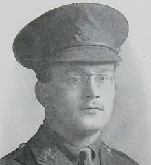 Head and shoulders of a man dressed in WW1 uniform wearing rounded glasses 